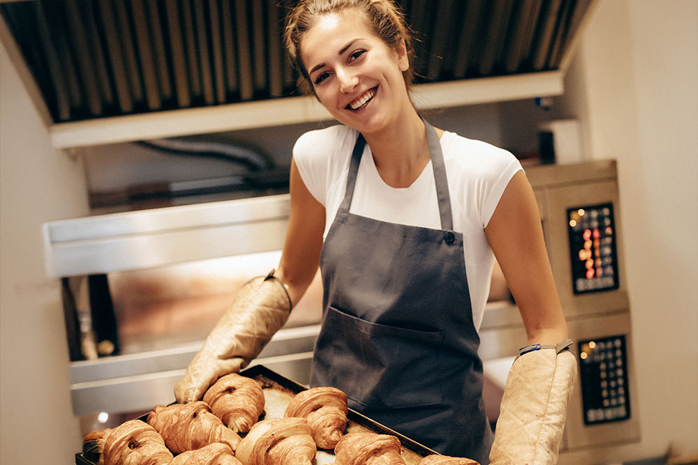 Bäckerin in der Backstube, die ein Backblech mit frischen Croissants hält